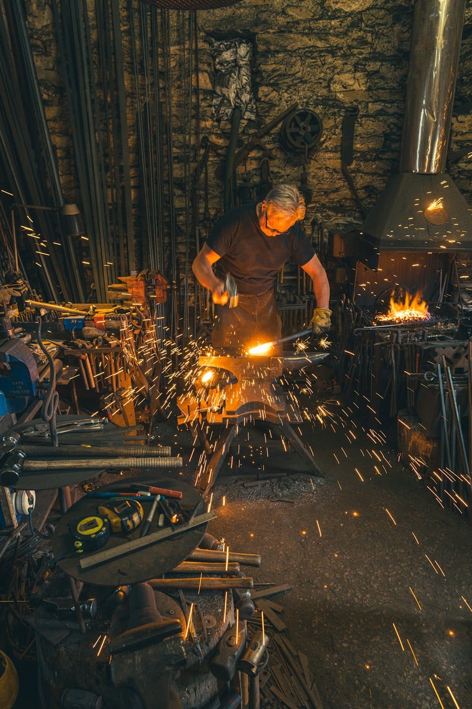 Blacksmith hammers glowing metal sparks fly from anvil.