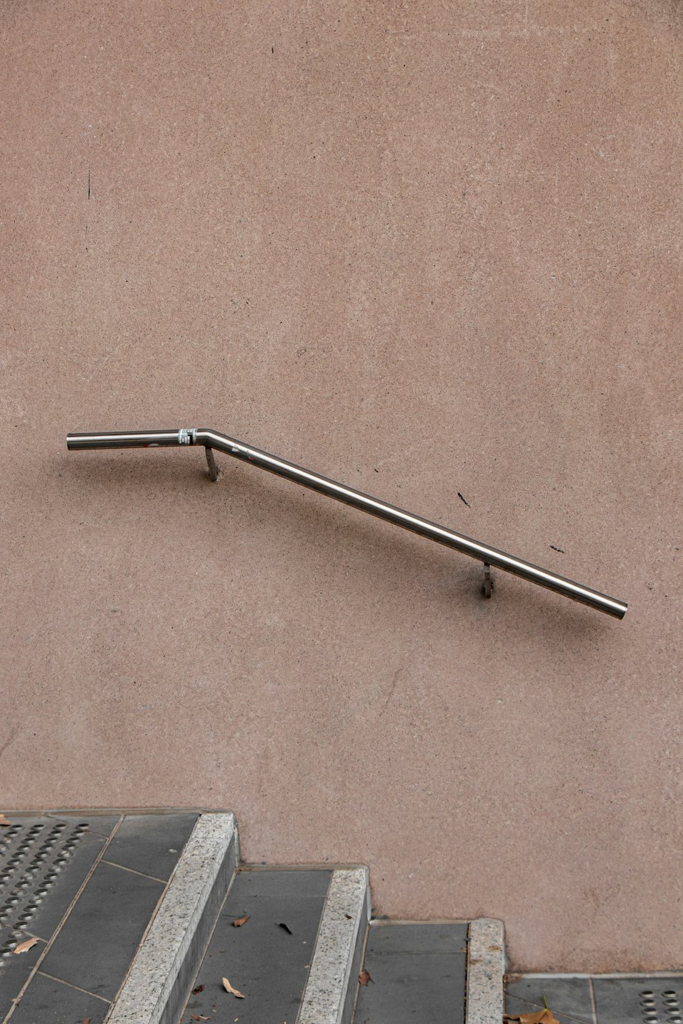 Stainless steel handrail mounted on a textured stucco wall.