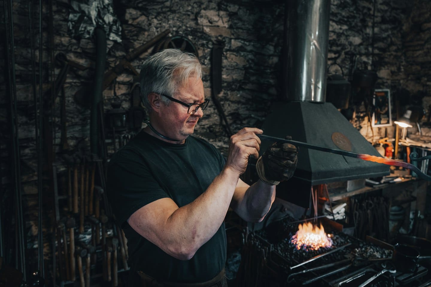 Blacksmith uses tongs to shape hot metal at a forge.